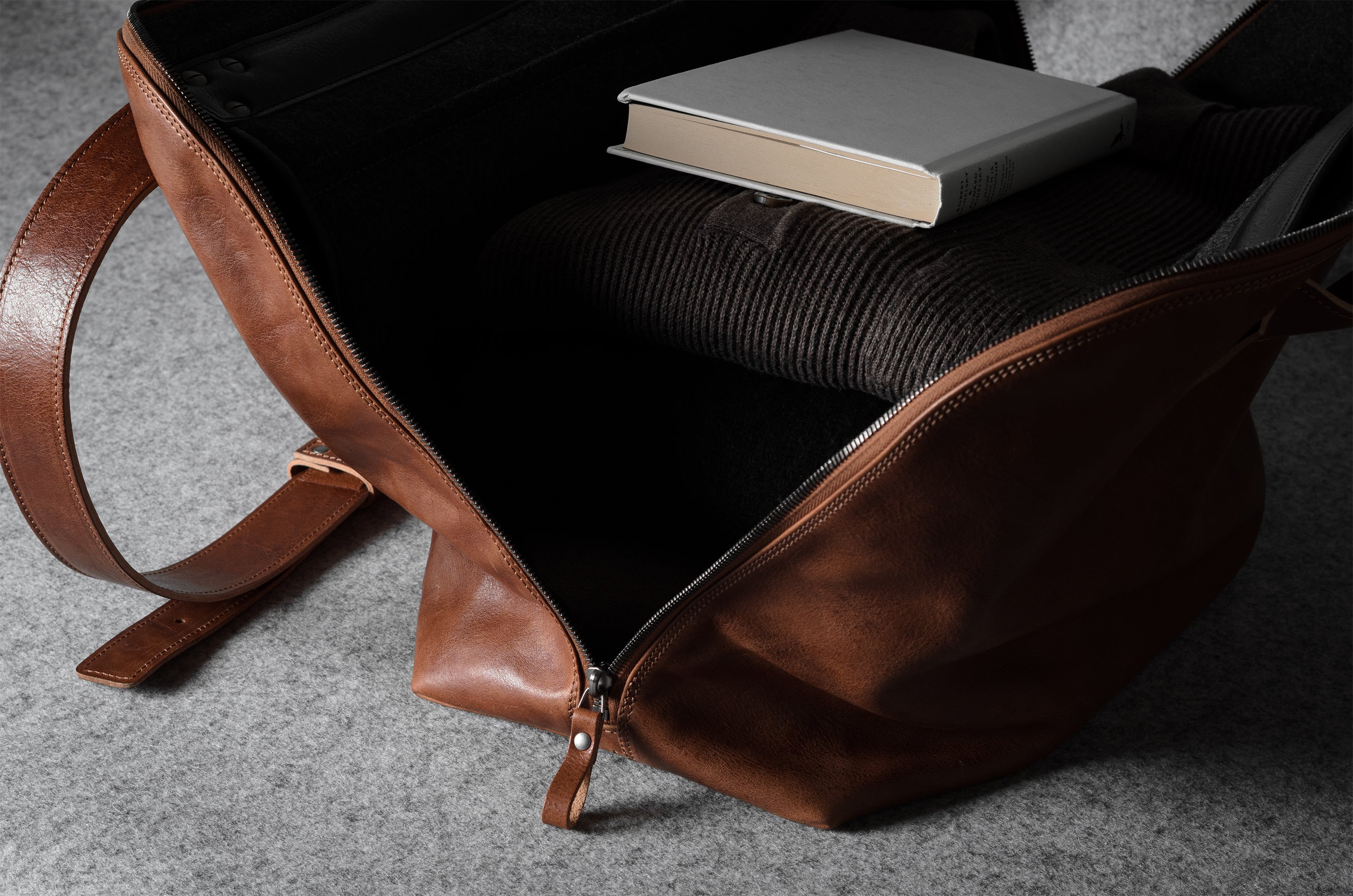 Brown leather bag with a book and sweater on a gray surface