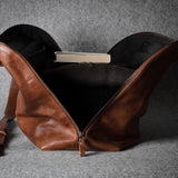 Brown leather bag with a grey interior, showing a sweater and book on a gray background