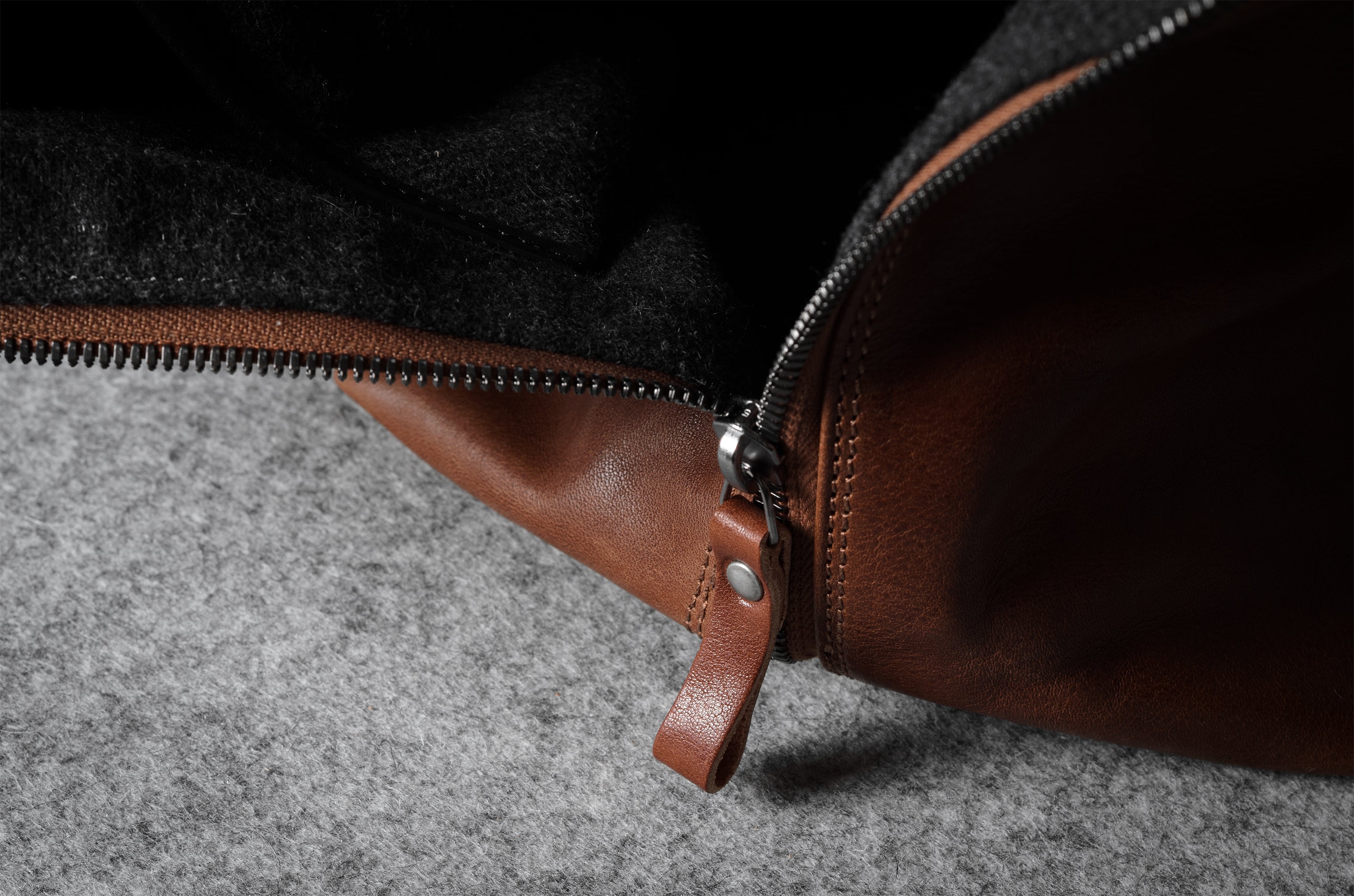 Close-up of a brown leather bag zipper on a dark fabric background