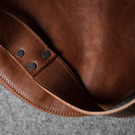 Close-up of a brown leather bag with visible stitching on a gray surface