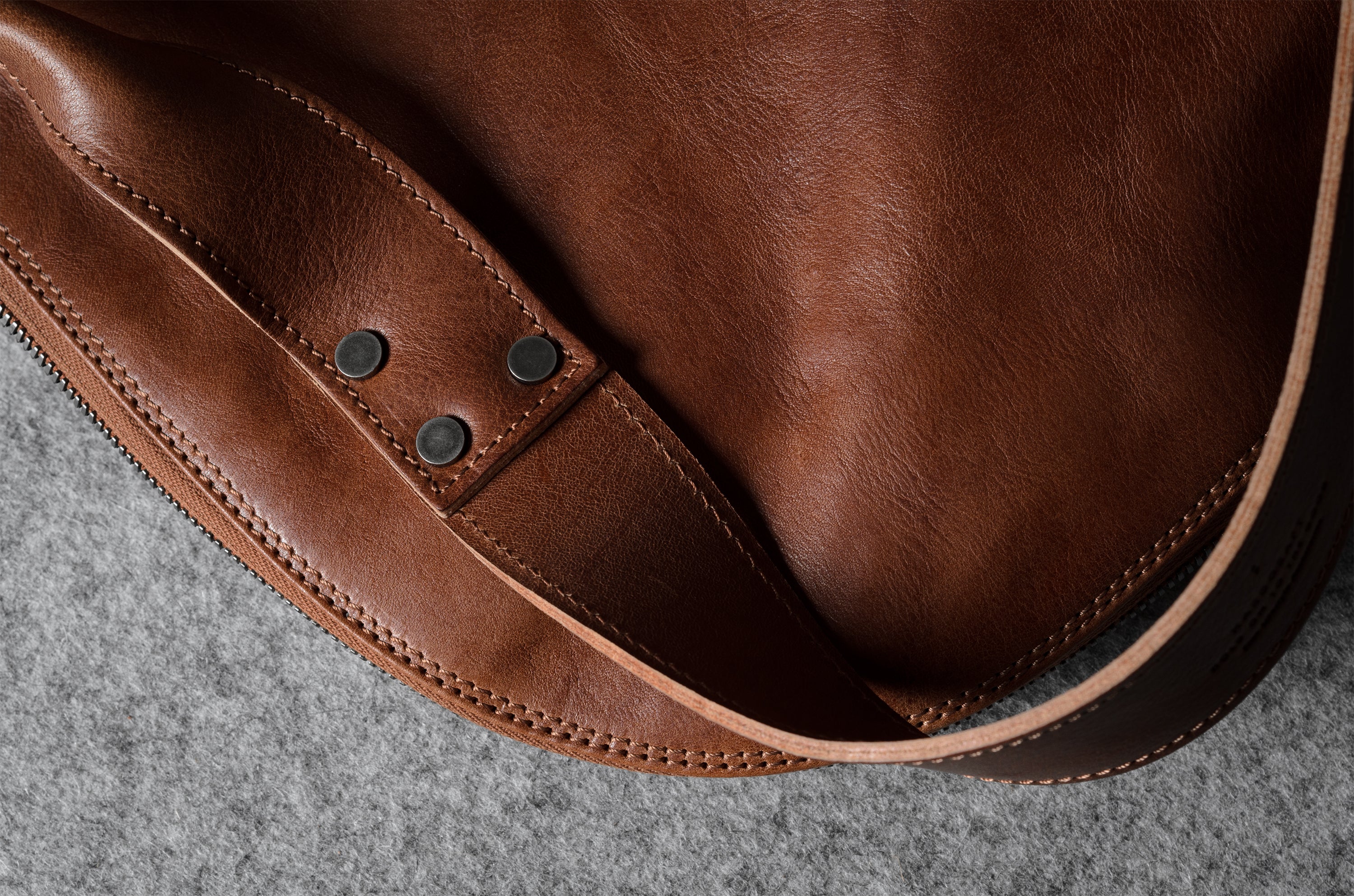 Close-up of a brown leather bag with visible stitching on a gray surface