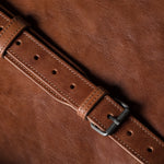 Close-up of a brown leather belt with a buckle on a brown background