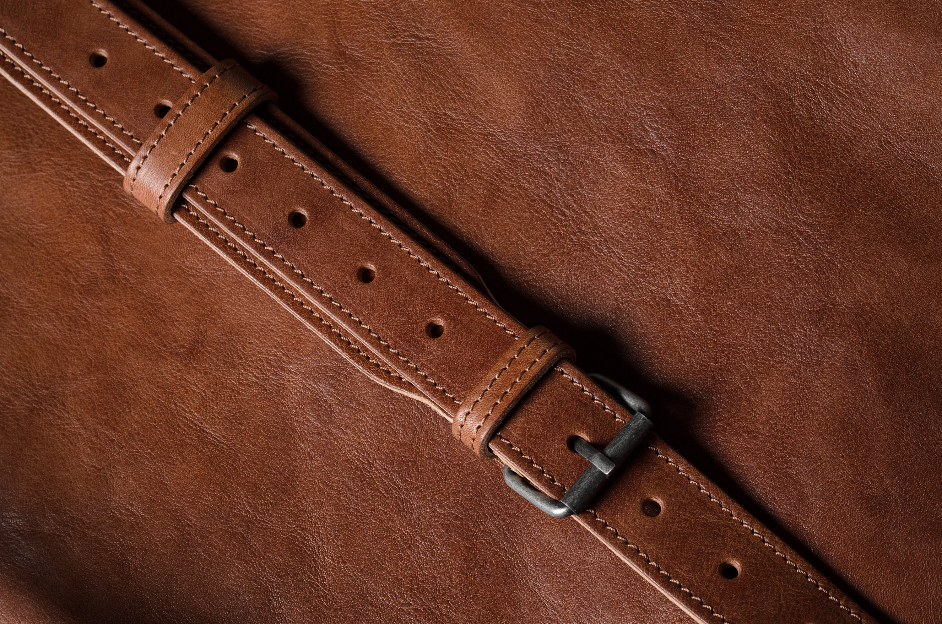 Close-up of a brown leather belt with a buckle on a brown background