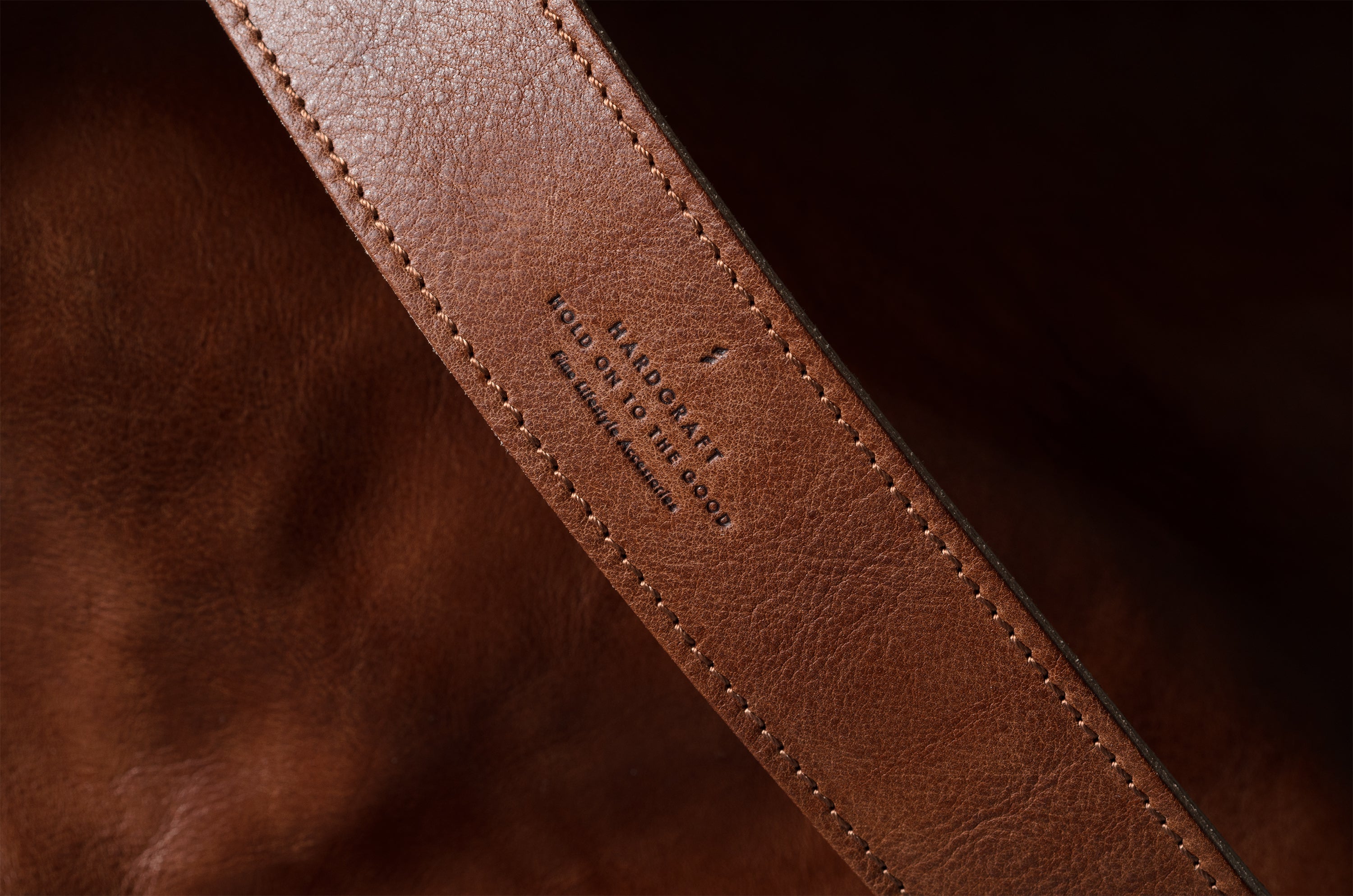 Close-up of a brown leather strap with visible branding on a dark background