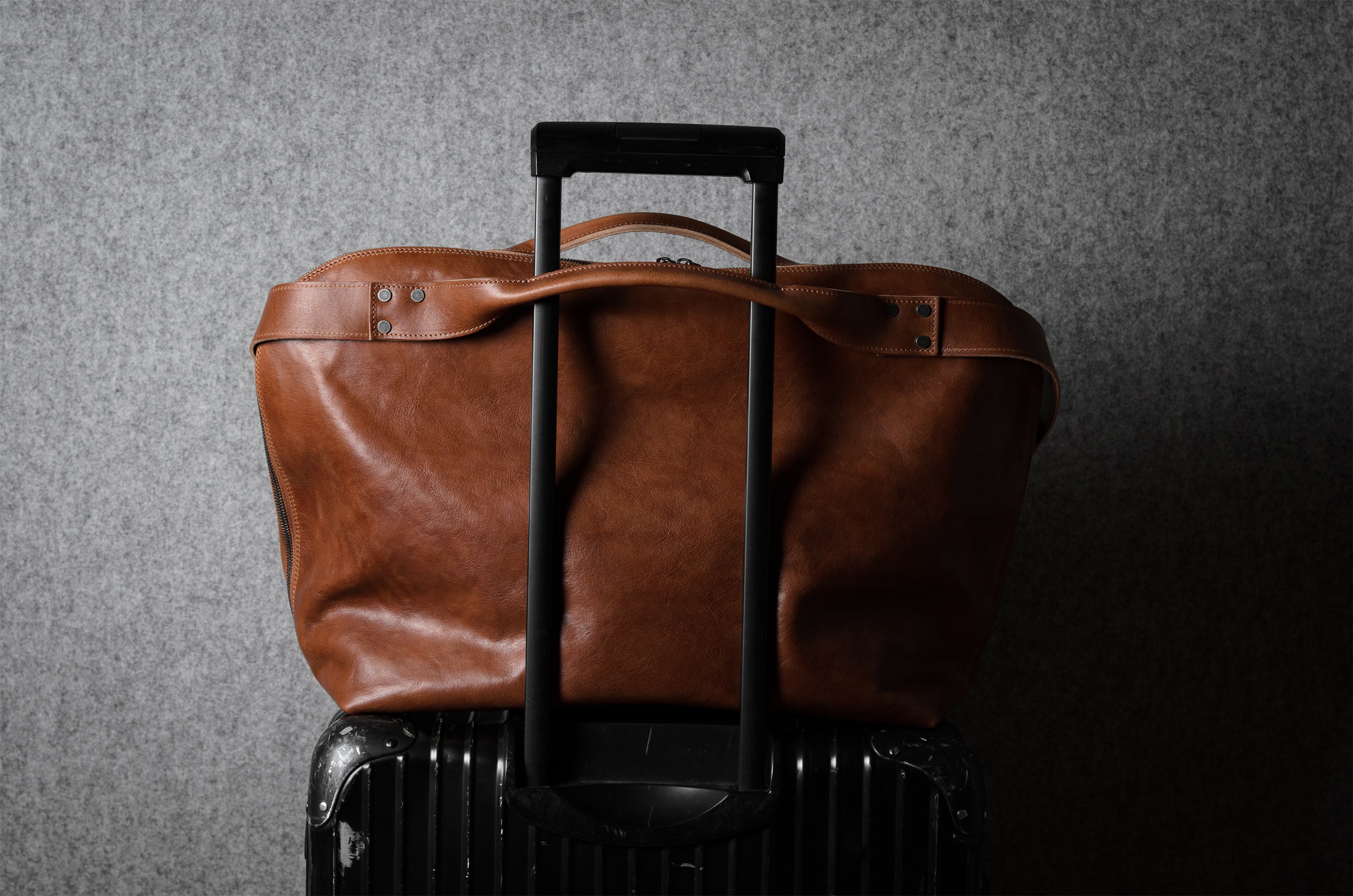 Brown leather duffel bag on a black suitcase against a gray background
