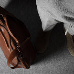 Brown leather bag on a gray surface with a person wearing shoes in the background