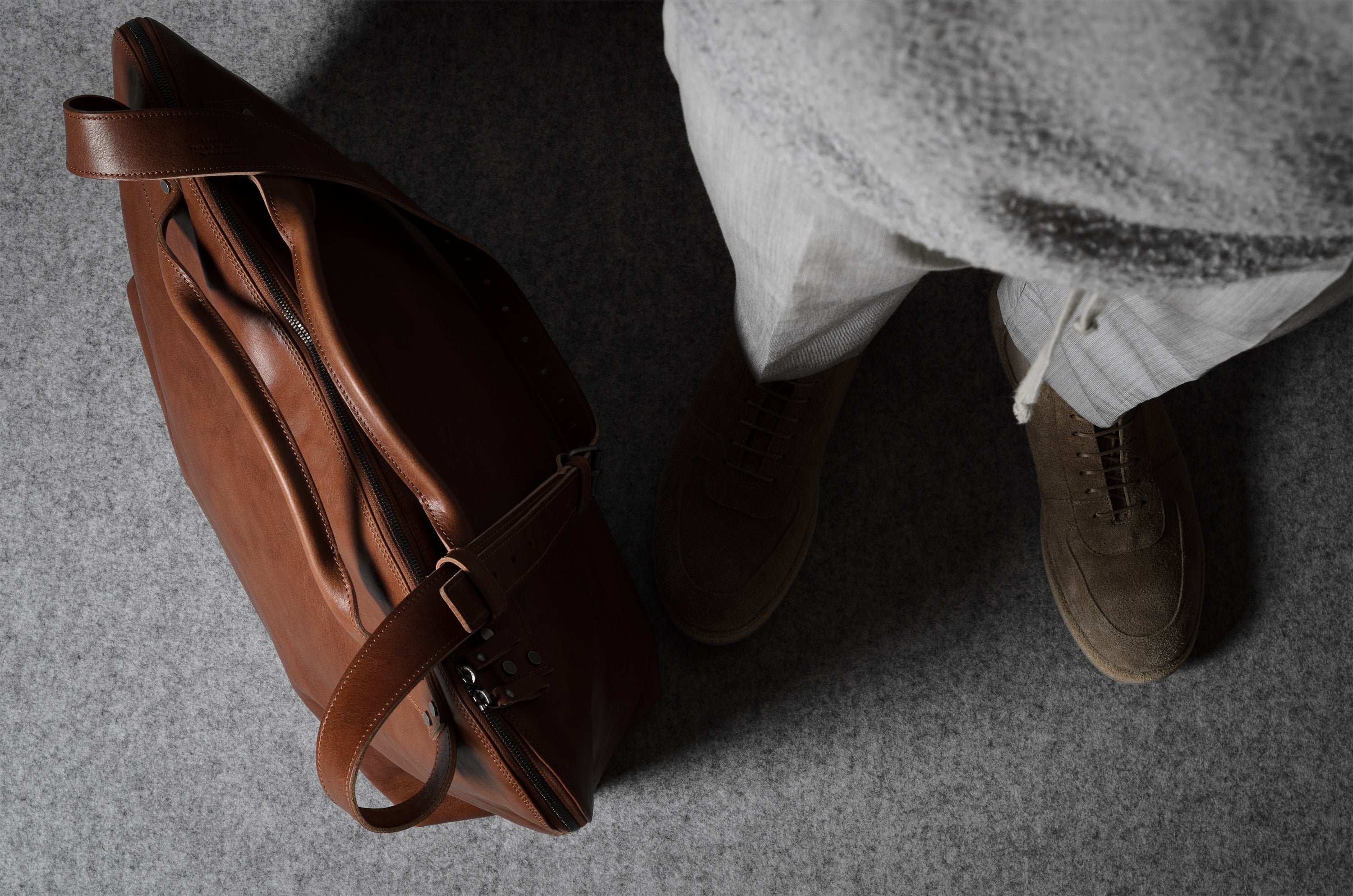 Brown leather bag on a gray surface with a person wearing shoes in the background