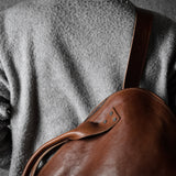 Person wearing a brown leather bag over their shoulder against a dark background