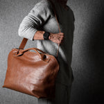 Person holding a brown leather bag against a dark background