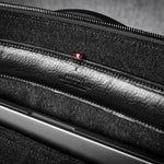 Close-up of a black leather bag interior with a laptop in pocket, zipper, showing texture and stitching details.