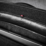 Close-up of a black leather bag interior with a laptop in pocket, zipper, showing texture and stitching details.