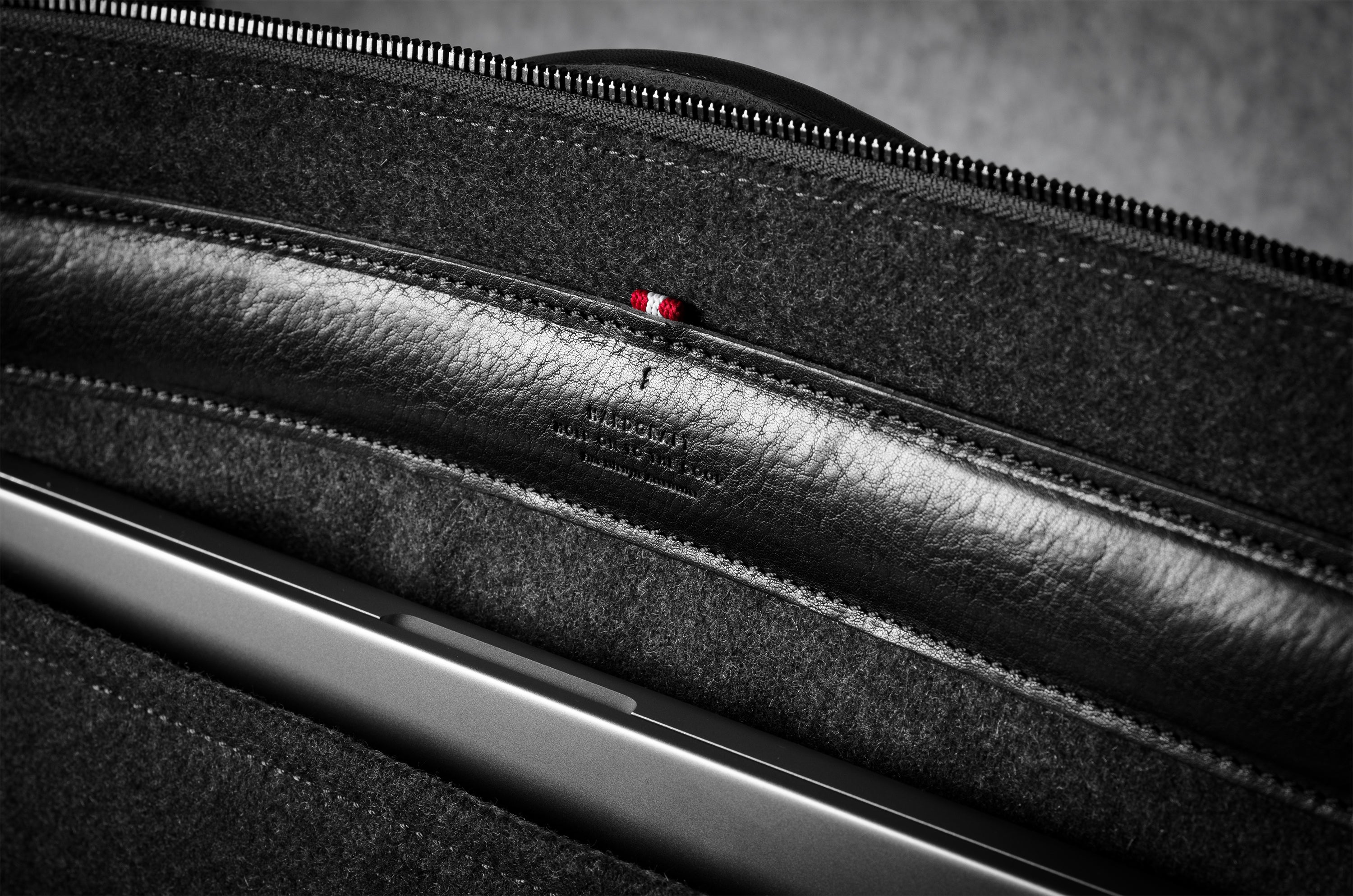 Close-up of a black leather bag interior with a laptop in pocket, zipper, showing texture and stitching details.