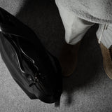 Person wearing a black leather jacket and brown shoes on a gray floor.