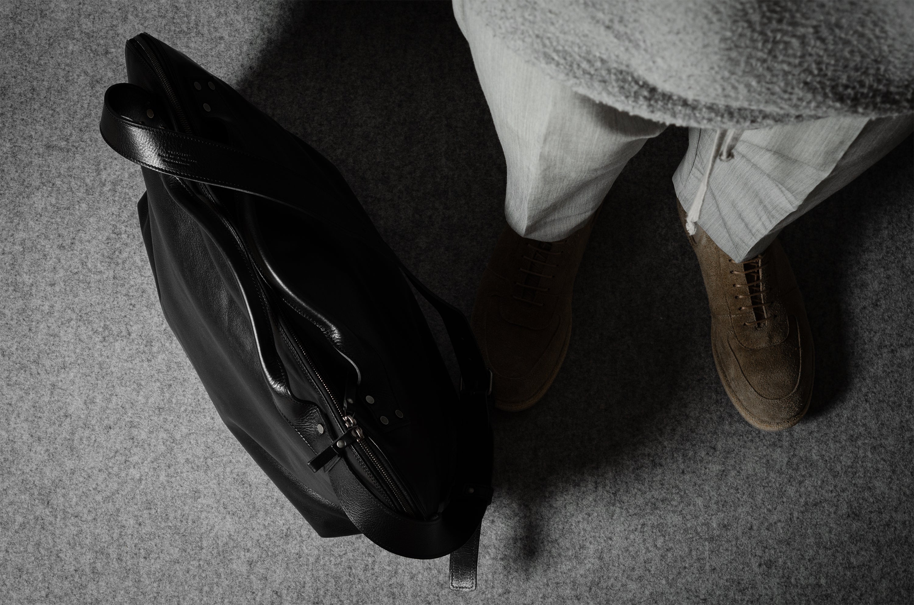 Person wearing a black leather jacket and brown shoes on a gray floor.