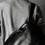Person wearing a textured wool sweater holding a leather bag against a plain background