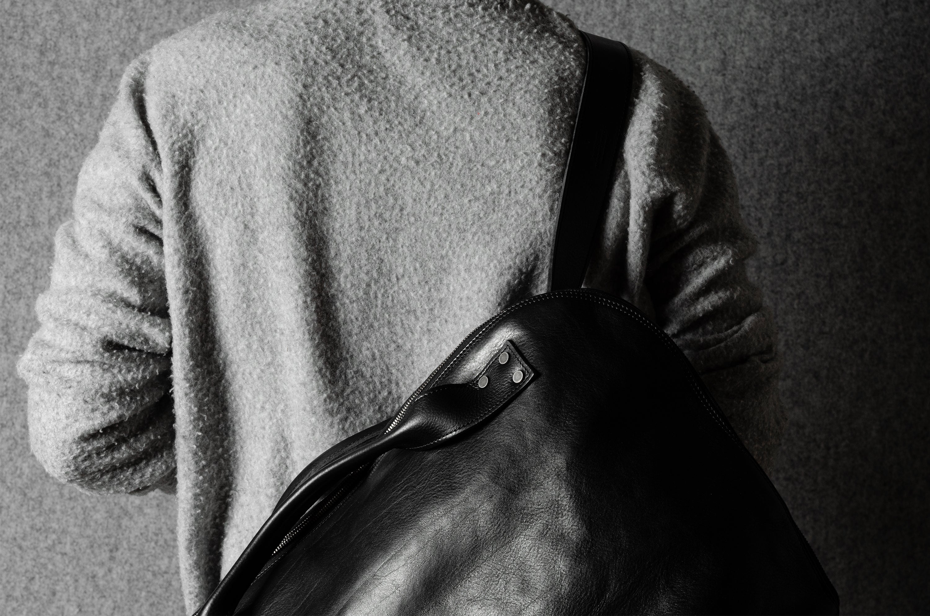 Person wearing a textured wool sweater holding a leather bag against a plain background