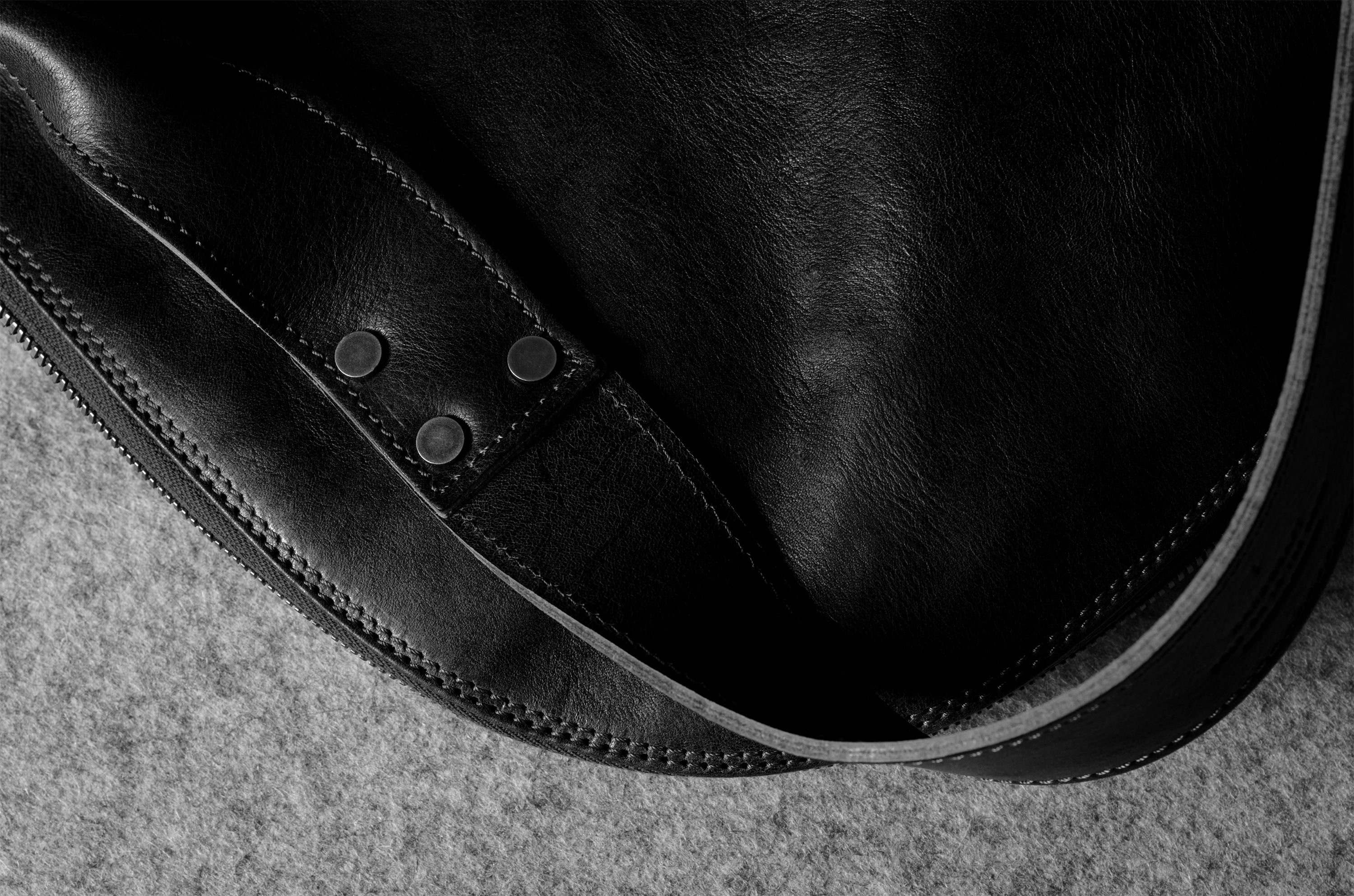 Close-up of a black leather bag with visible stitching on a textured surface