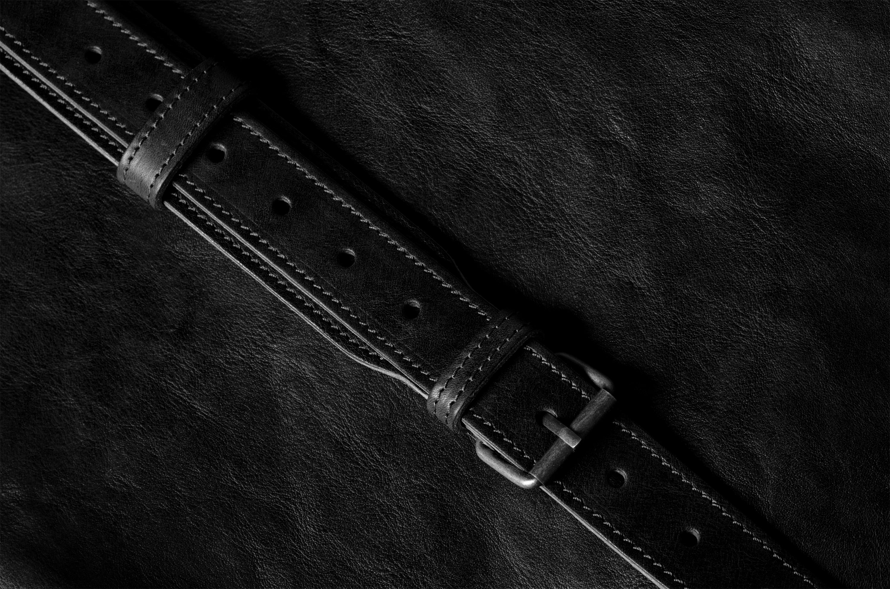Close-up of a black leather belt on a dark textured surface