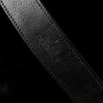 Close-up of a black leather belt with visible stitching on a black background