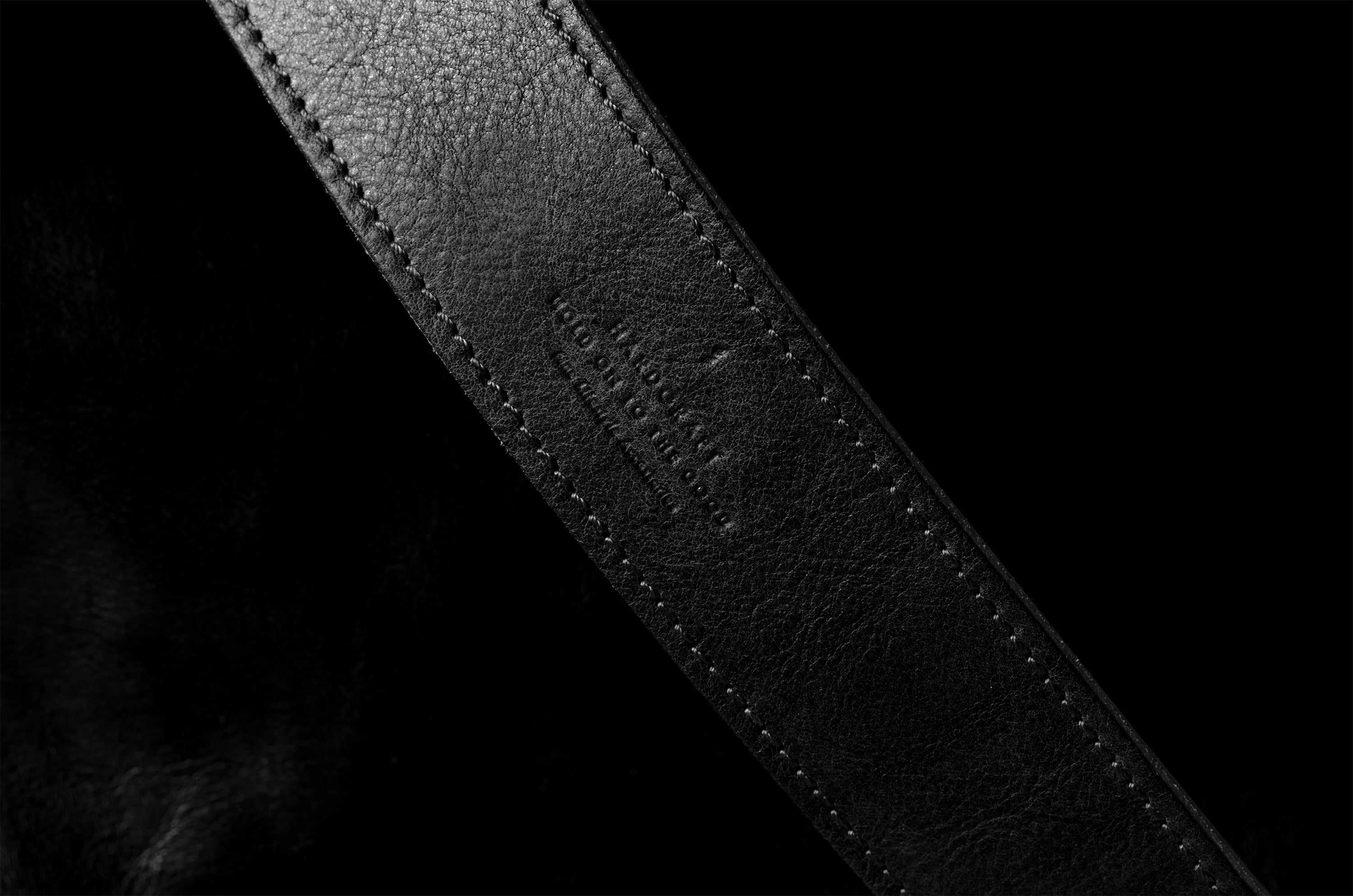 Close-up of a black leather belt with visible stitching on a black background