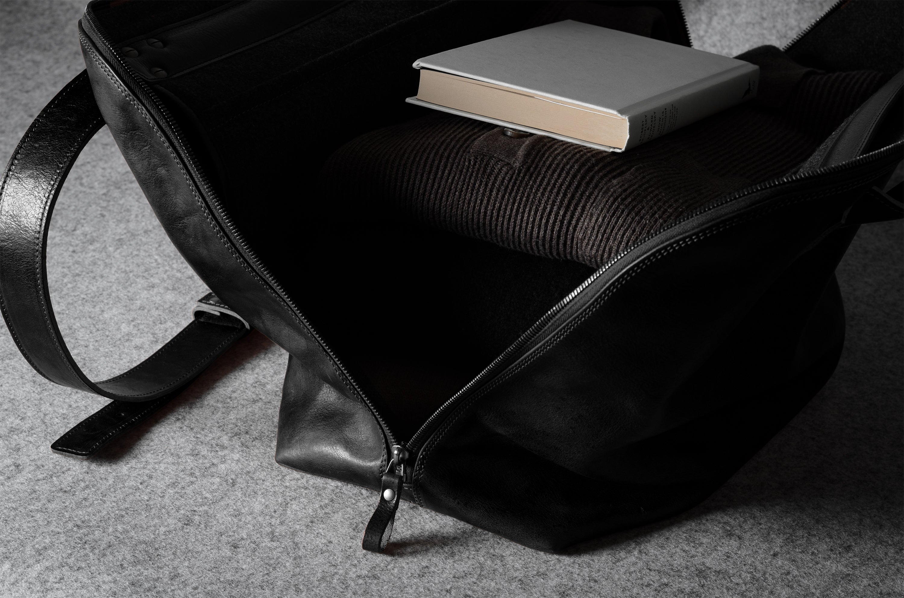 Black leather bag with a book on a gray surface