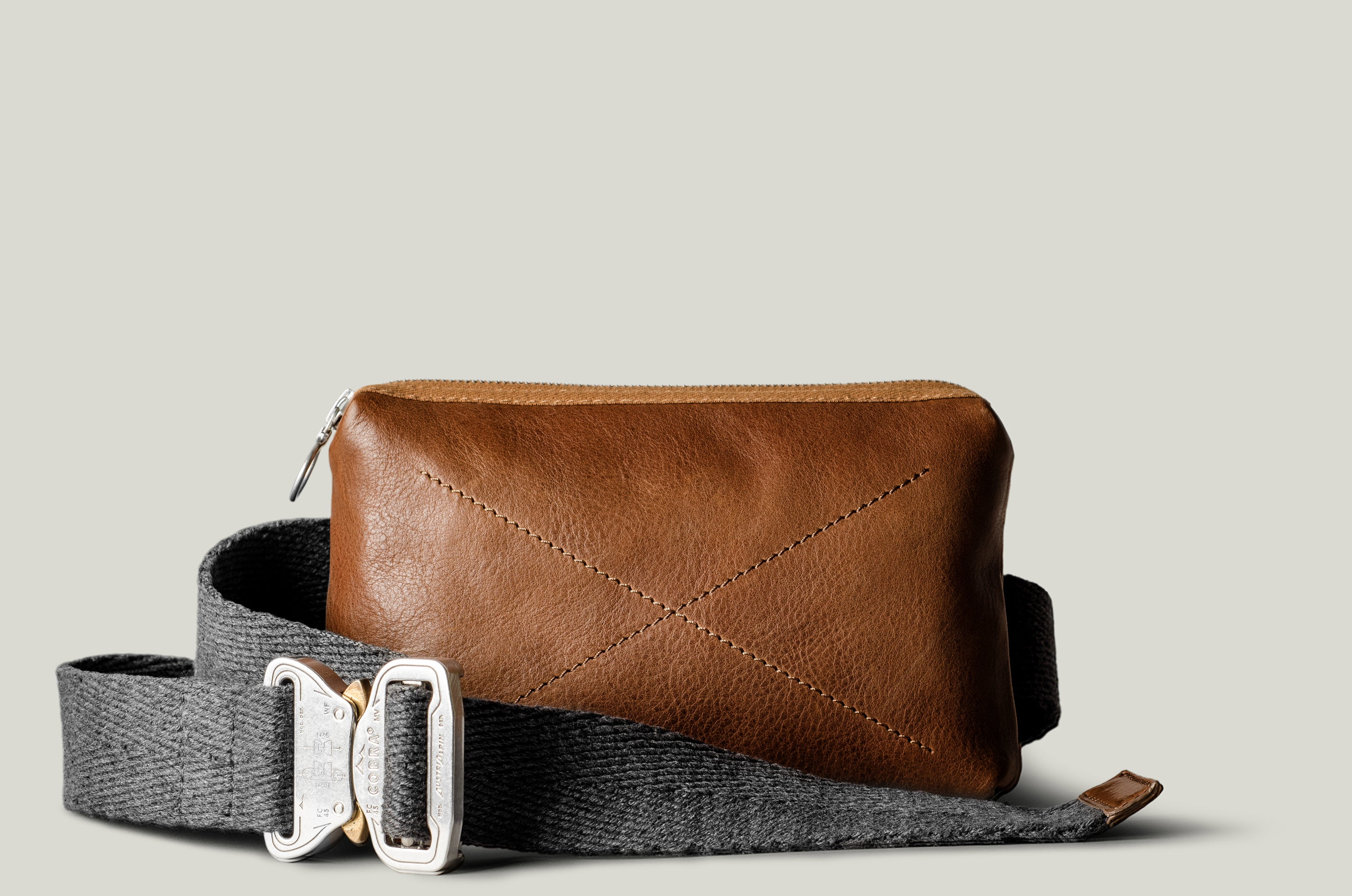 Brown leather bag with a gray strap on a light beige background