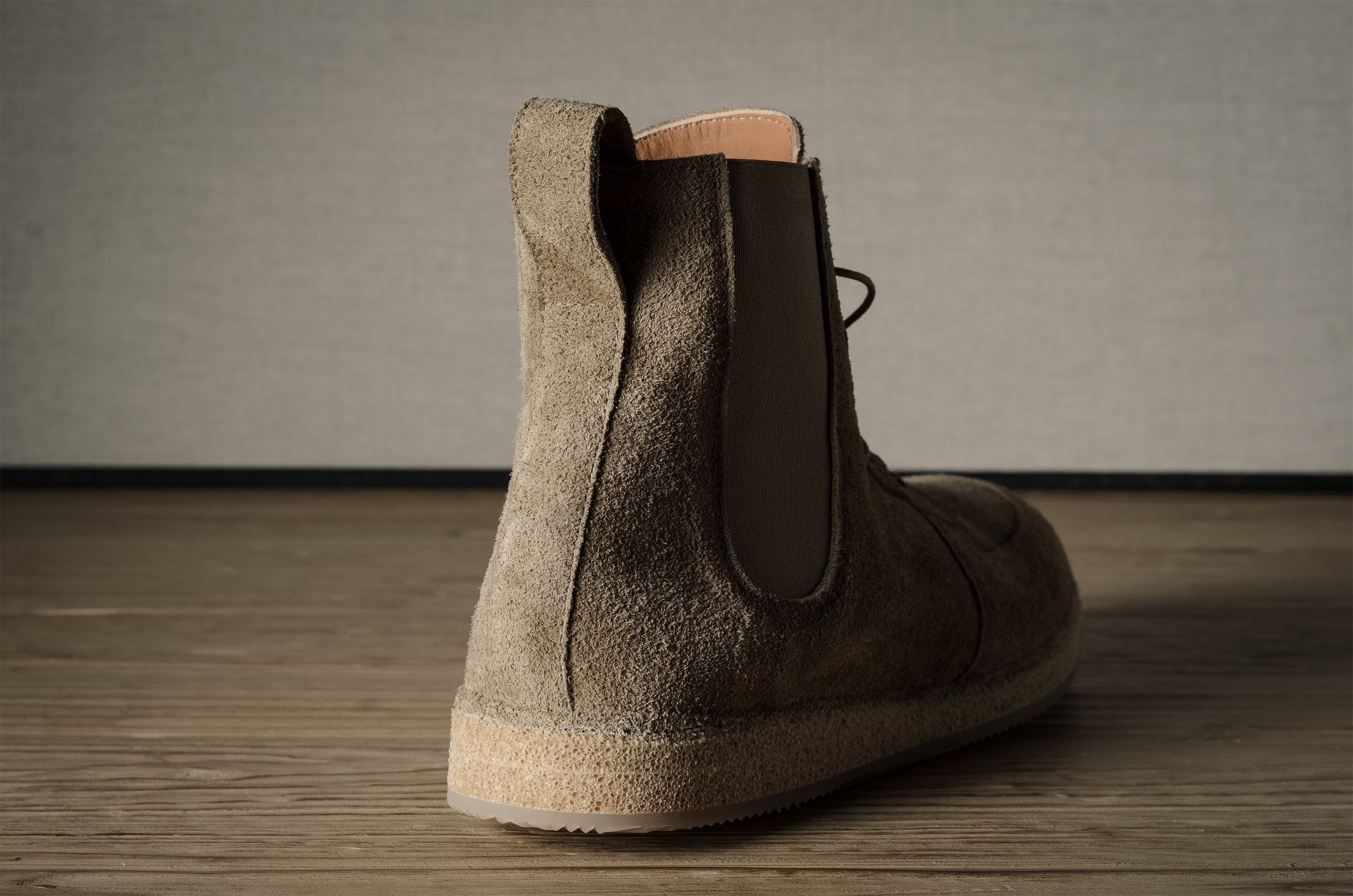 Brown suede boot on a wooden floor with a neutral background