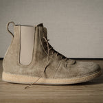 Brown suede boot on a wooden floor with a neutral background