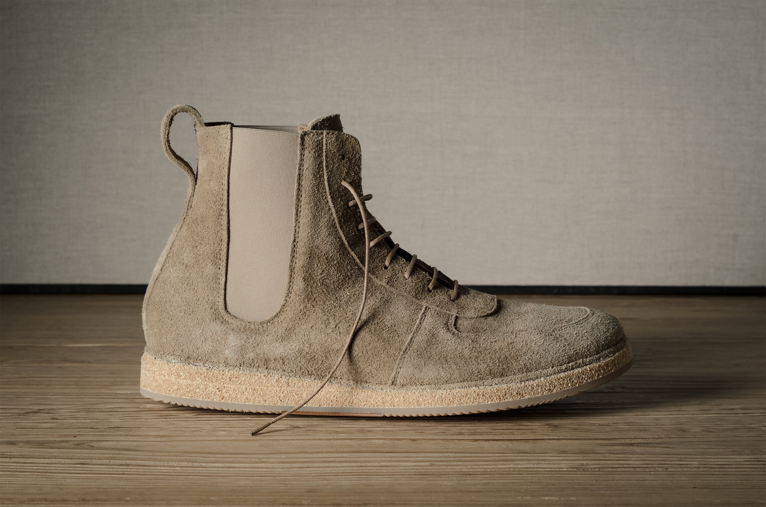 Brown suede boot on a wooden floor with a neutral background