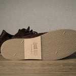 Brown leather shoes with a visible brand label on a wooden floor.