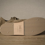 Close-up of a brown shoe with a textured sole on a wooden floor.