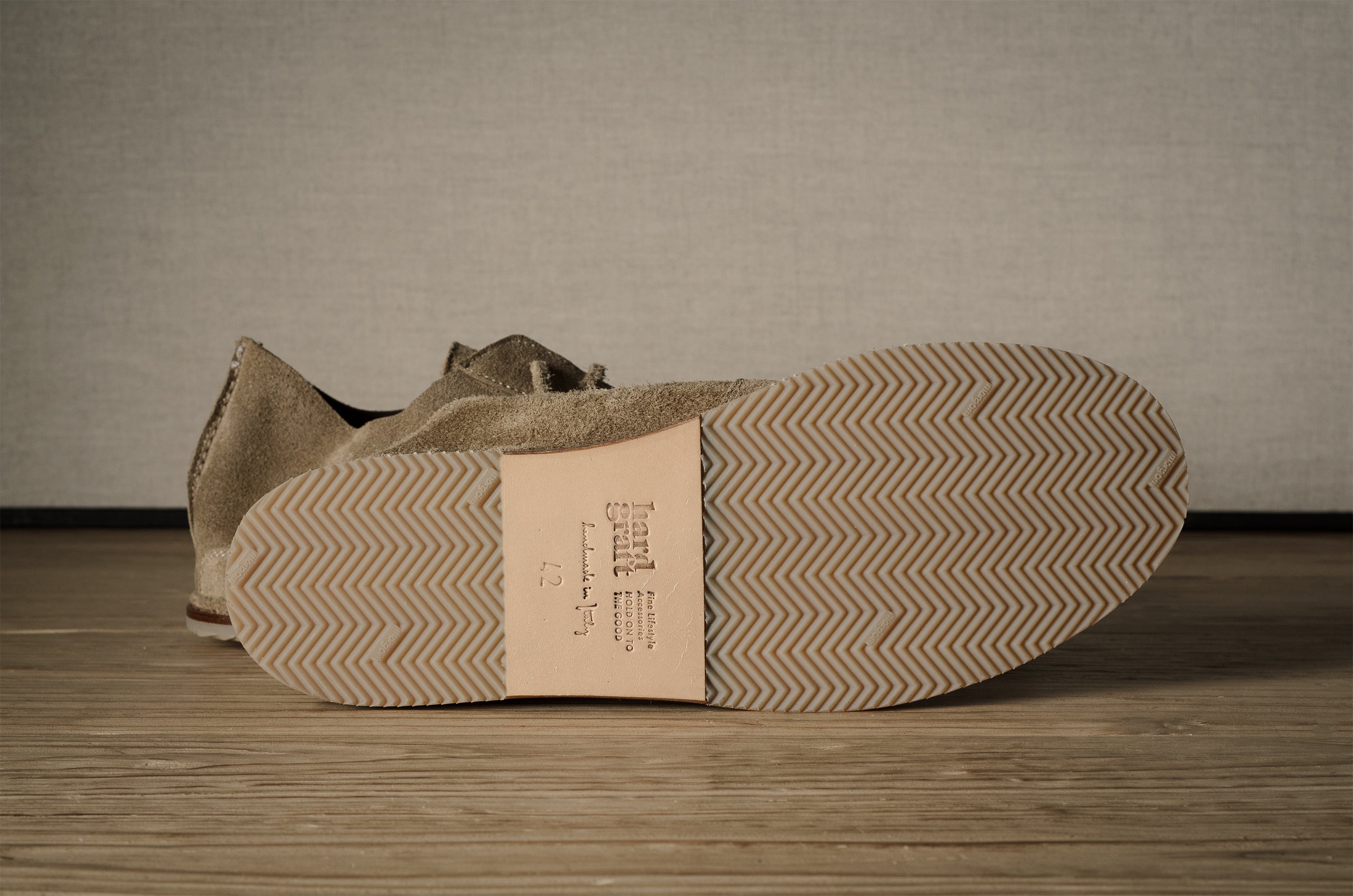 Close-up of a brown shoe with a textured sole on a wooden floor.