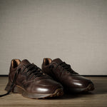 Pair of brown leather sneakers on a wooden floor with a neutral background