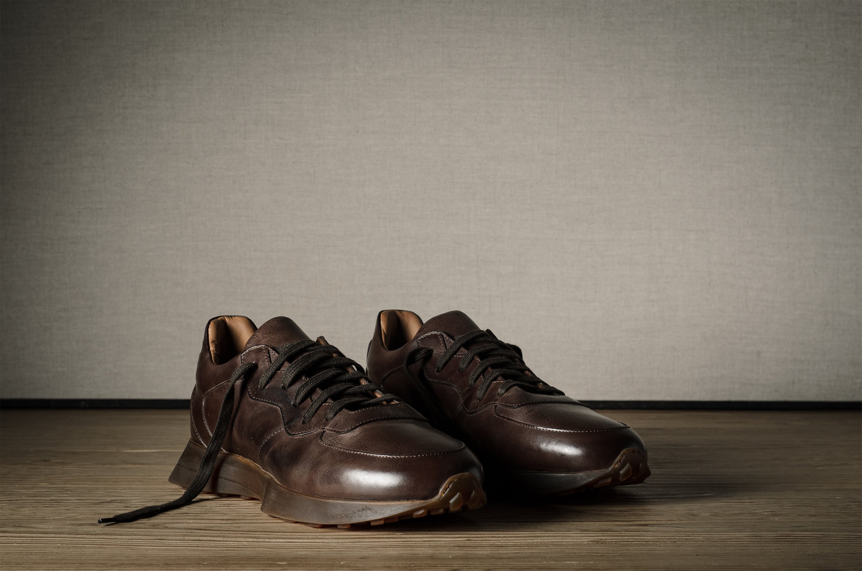 Pair of brown leather sneakers on a wooden floor with a neutral background
