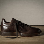 Pair of brown leather sneakers on a wooden floor with a neutral background