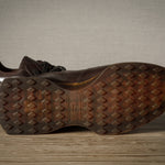 Brown leather sneakers with textured sole on a wooden surface