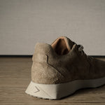 Brown suede sneaker on a wooden floor with a neutral background