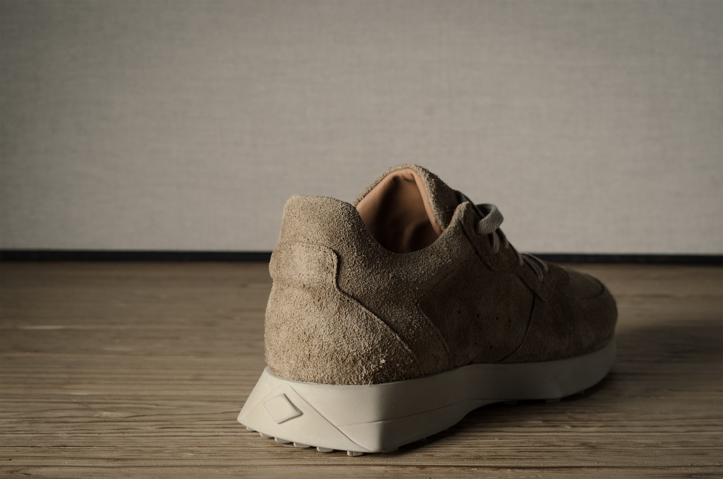 Brown suede sneaker on a wooden floor with a neutral background