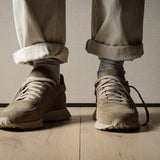 Close-up of a person wearing beige sneakers and rolled-up pants on a wooden floor.
