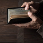 Person holding a black leather passport case on a wooden surface