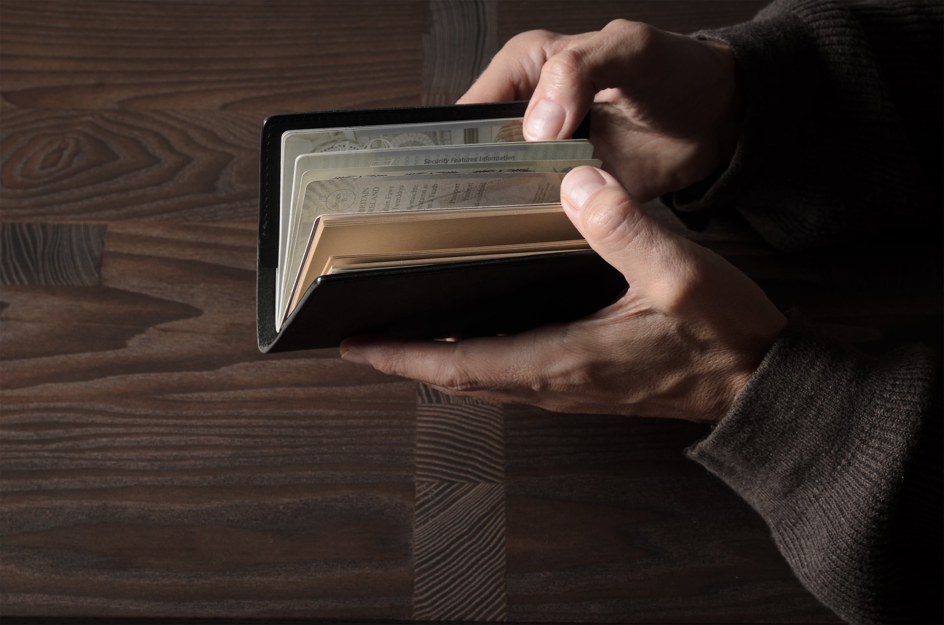 Person holding a black leather passport case on a wooden surface