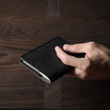 Person holding a black leather passport case on a wooden surface