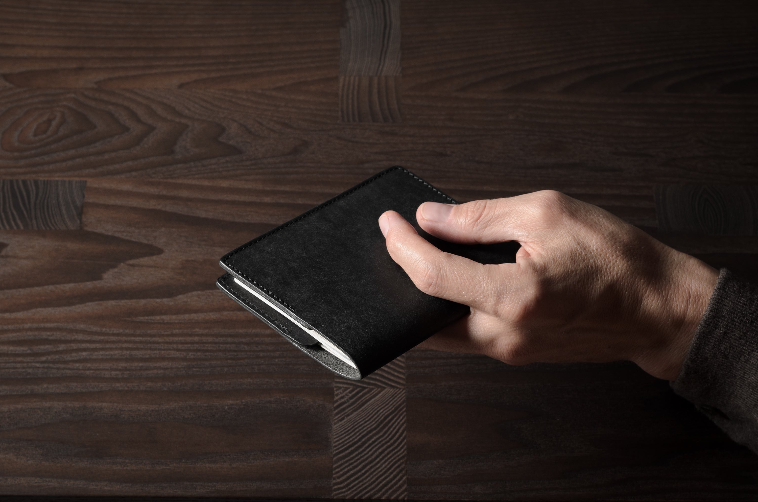 Person holding a black leather passport case on a wooden surface