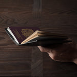 Person holding a black leather passport case on a wooden surface