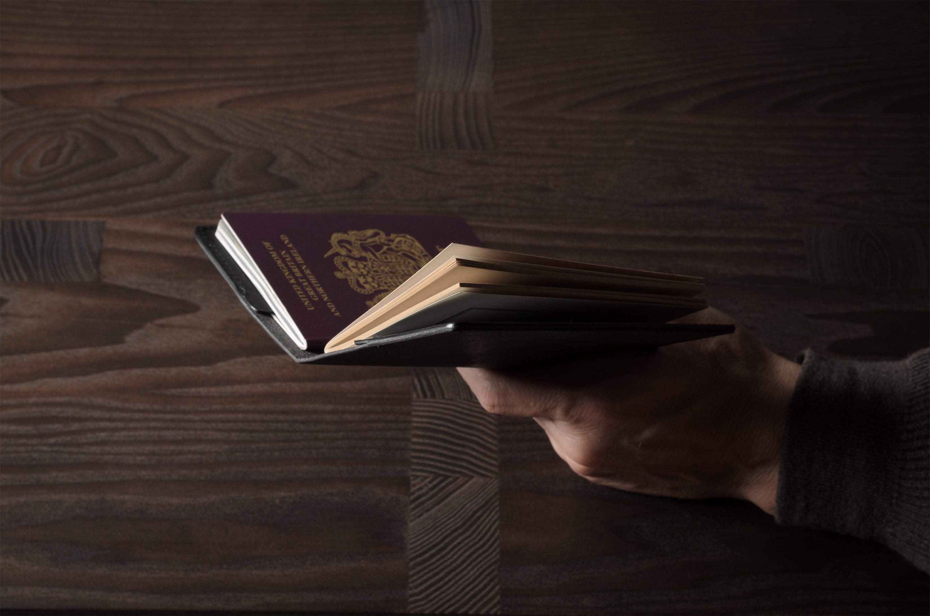 Person holding a black leather passport case on a wooden surface