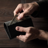 Person holding a black leather passport case on a wooden surface