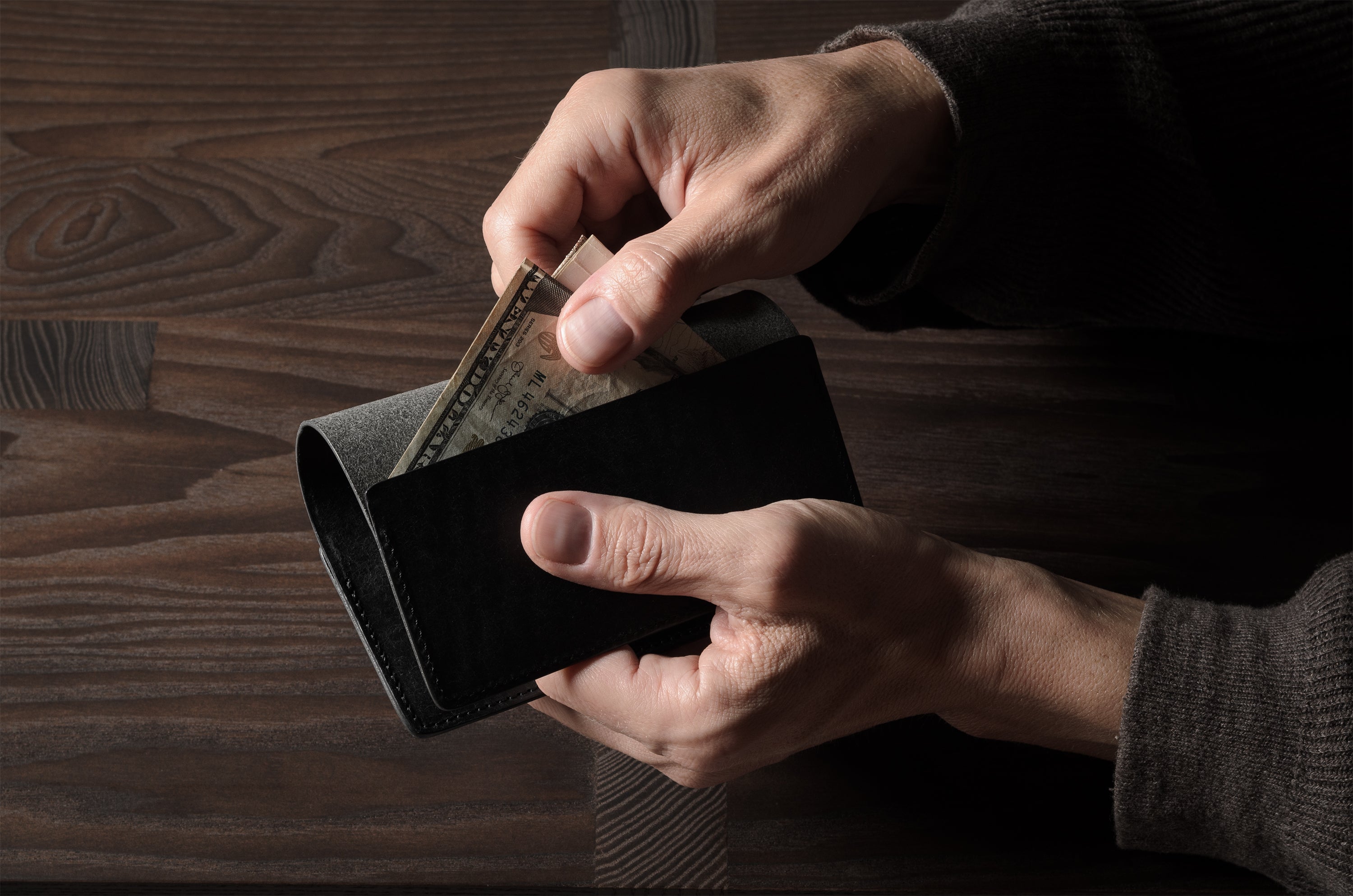 Person holding a black leather passport case on a wooden surface