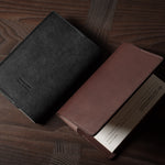Two leather passport wallets, one black and one brown, on a wooden surface.