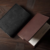 Two leather passport wallets, one black and one brown, on a wooden surface.