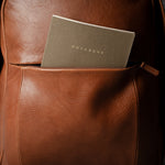 Brown leather backpack with a notebook inside on a dark background